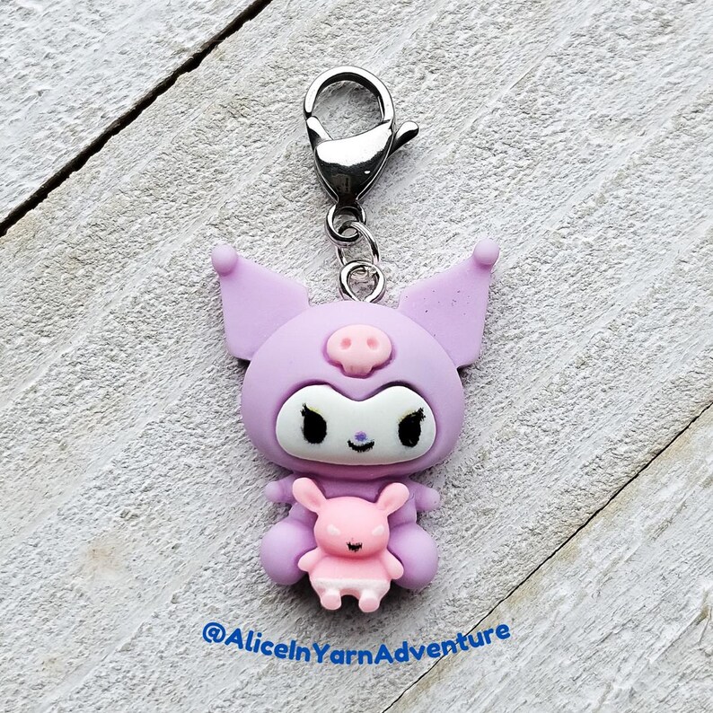 May include: A purple and white character with pig ears and a pink piglet in its arms. The character is attached to a silver charm loop. The character is a popular Japanese cartoon character.