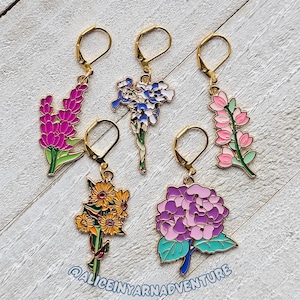 May include: Five gold-tone flower charm earrings with a hook fastening. The charms feature a variety of flowers, including purple and pink wildflowers, blue irises, yellow sunflowers, and a pink hydrangea.