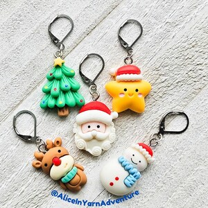 May include: A selection of festive keyrings with Christmas designs. The keyrings depict a green Christmas tree, a yellow star, Santa Claus, a reindeer, and a snowman. Each charm has a silver clasp. The text "@AliceinYarnAdventure" is visible.