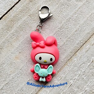 May include: Pink Hello Kitty charm with a blue bunny in her arms. The charm is attached to a silver key ring.