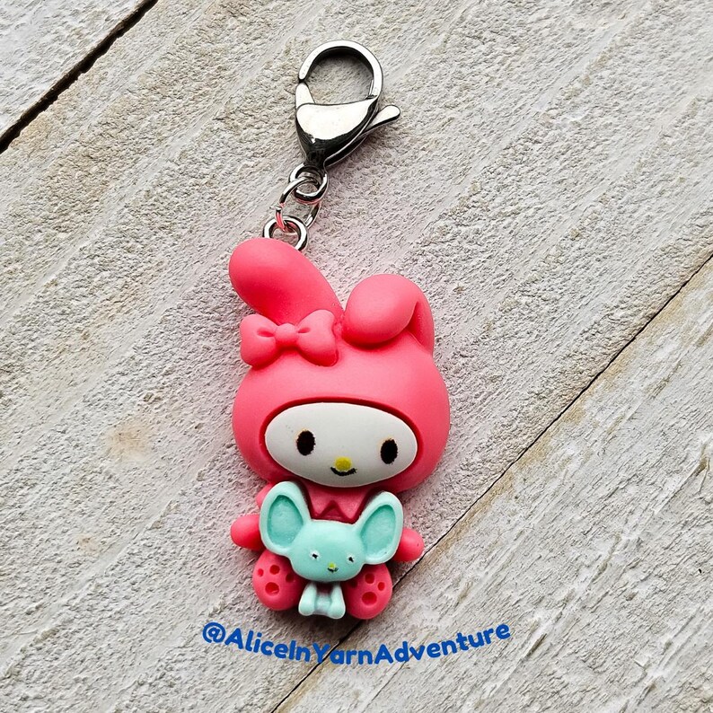 May include: Pink Hello Kitty charm with a blue bunny in her arms. The charm is attached to a silver key ring.