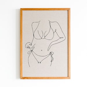 May include: A framed line drawing of a person in a bikini. The drawing is in black ink on a beige canvas.