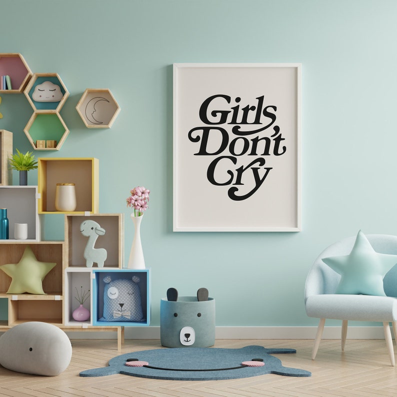 Puede incluir: Una habitaci&oacute;n infantil azul claro con una impresi&oacute;n enmarcada en blanco que dice "Girls Don't Cry" en letras negras. Hay un sill&oacute;n azul con una almohada azul claro y una almohada en forma de estrella. Hay una estanter&iacute;a de madera con una variedad de art&iacute;culos coloridos, incluyendo una jirafa de peluche, una almohada en forma de estrella y un jarr&oacute;n con flores rosas.
