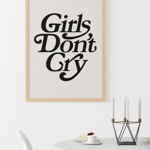 Puede incluir: Una impresi&oacute;n enmarcada con el texto "Girls Don't Cry" en un estilo de fuente retro. La impresi&oacute;n est&aacute; sobre un fondo beige claro y est&aacute; enmarcada en un marco de madera claro. La impresi&oacute;n est&aacute; colgada en una pared blanca.
