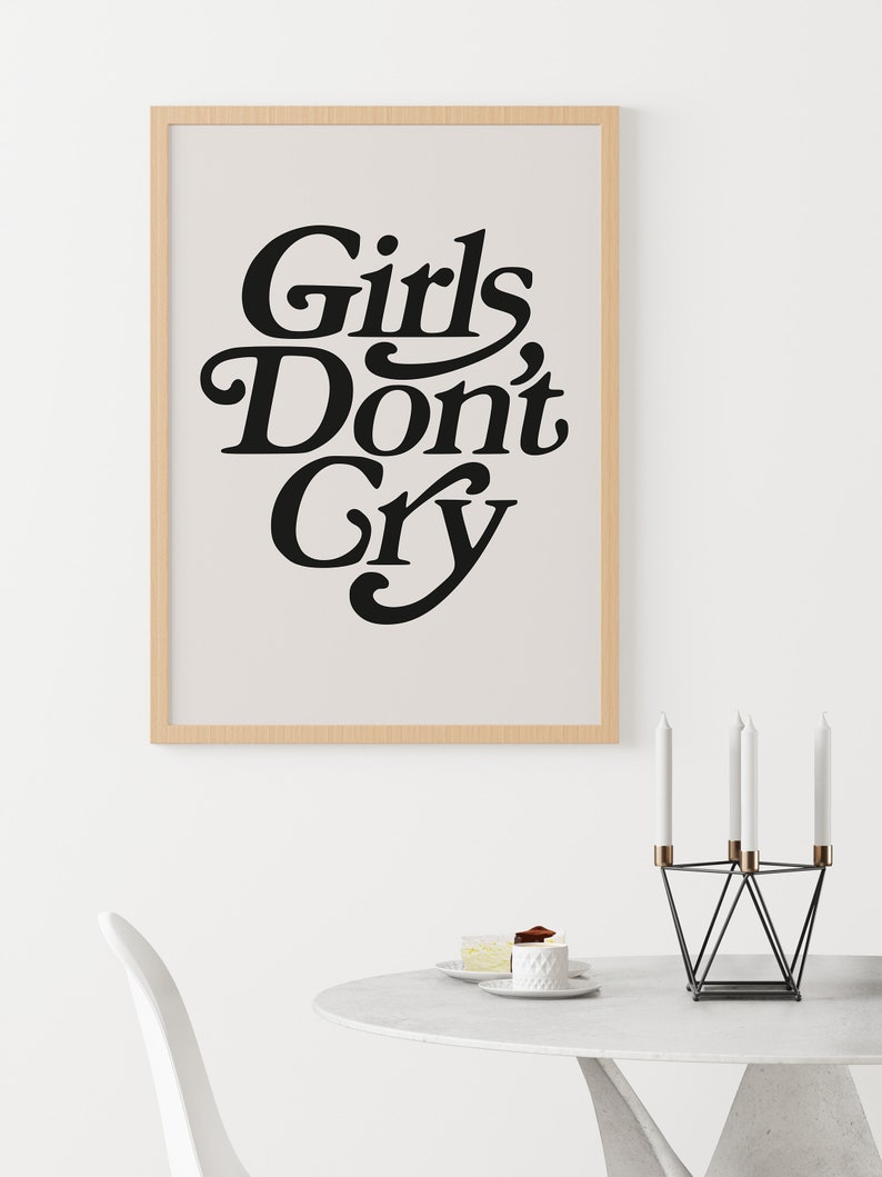 Puede incluir: Una impresi&oacute;n enmarcada con el texto "Girls Don't Cry" en un estilo de fuente retro. La impresi&oacute;n est&aacute; sobre un fondo beige claro y est&aacute; enmarcada en un marco de madera claro. La impresi&oacute;n est&aacute; colgada en una pared blanca.