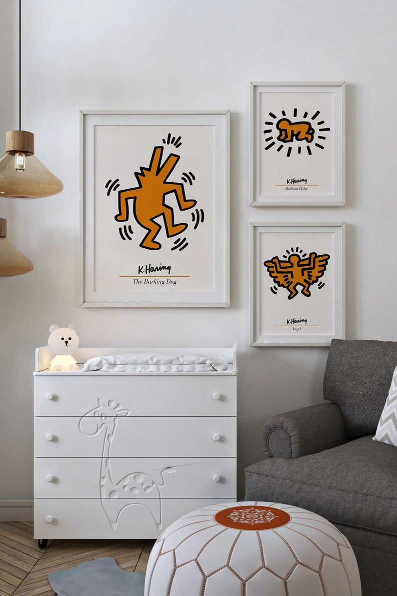 May include: A white dresser with four drawers features a giraffe design. The dresser is next to a white pouf with an orange center. Three framed prints with black outlines and orange figures are on the wall. The prints are by K. Haring and feature the titles "The Barking Dog", "Radiant Baby", and "Angel".