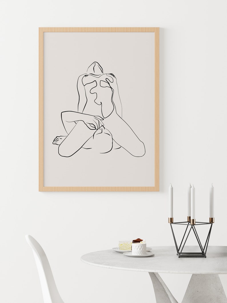 Peut inclure: Un dessin au trait noir et blanc d'une personne assise, les jambes crois&eacute;es. Le dessin est encadr&eacute; dans un cadre en bois clair et est accroch&eacute; &agrave; un mur blanc.