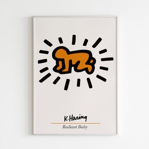 May include: A framed print of a black and orange illustration of a baby with a radiating sunburst around it. The print is titled "Radiant Baby" and signed "K. Haring".