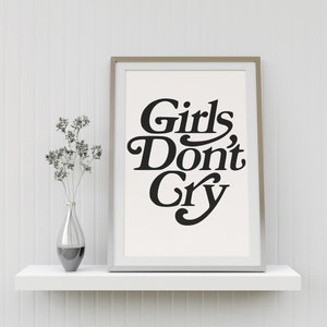 Puede incluir: Una impresi&oacute;n enmarcada con el texto "Girls Don't Cry" en una fuente en negrita y estilizada. La impresi&oacute;n est&aacute; sobre un fondo blanco y est&aacute; enmarcada en un marco plateado. La impresi&oacute;n est&aacute; sentada en un estante blanco contra una pared blanca.