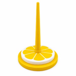 May include: A bright yellow ring holder featuring a tall, tapered central cone rising from a circular base. The base is decorated with a white and yellow citrus slice pattern, resembling a lemon or orange, with distinct segments radiating outward.