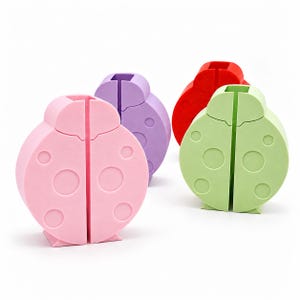 May include: A set of four ladybird-shaped silicone cord organisers in pink, purple, red, and light green. Each circular holder features a vertical slit down the centre and embossed circular spots on the surface, designed to keep cables organised.