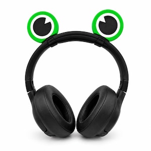 May include: Black over-ear headphones featuring a headband adorned with two circular green and black frog-eye attachments. The headphones have a padded black headband and two large, cushioned black ear cups designed for audio listening.