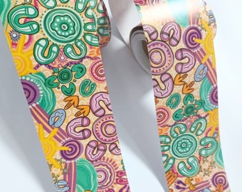 May include: A roll of patterned washi tape featuring an Aboriginal Australian design with green, purple, orange, and yellow colors. The design includes circles, dots, and lines. The text "songlines x Banya" is visible on the tape.
