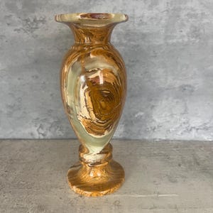 May include: A small, brown and white marble vase with a flared top and a round base.