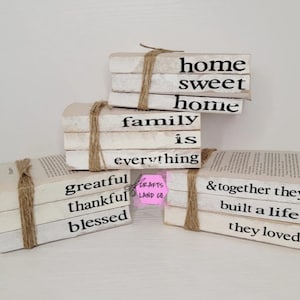 May include: Stack of white painted books with twine tied around them. The books have the following text printed on them: "home sweet home", "family is everything", "greatful thankful blessed", and "& together they built a life they loved".