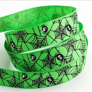 May include: Green ribbon with a black spider web and spider design. The spiders have black bodies and white eyes.