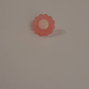 May include: A pink plastic flower button with a white centre.