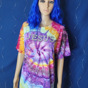May include: A tie-dye t-shirt with a rainbow swirl pattern. The shirt has the word "JESUS" spelled out in rhinestones.