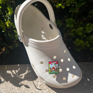 May include: White clog with a red and green Arnott's 'Toffee Pops' cereal box pin attached to the front.