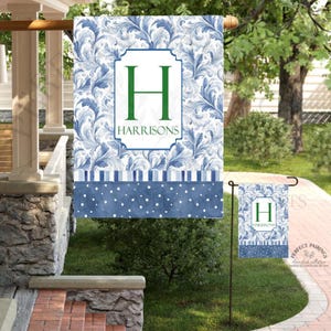 May include: A blue and white garden flag with a floral design and the name "HARRISONS" in a white frame. The letter "H" is in green. A smaller matching flag is in the foreground.