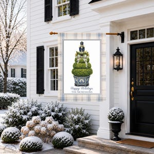 May include: A rectangular garden flag featuring a light blue and beige plaid border. The center displays a topiary tree in a blue and white patterned planter, topped with a nutcracker and a plaid bow. Text reads Happy Holidays THE MCKESSONS.