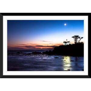 May include: A white lighthouse with a green roof sits on a rocky cliff overlooking the ocean. The sky is a deep blue with a sliver of moon visible. The water is calm and reflects the light from the lighthouse.