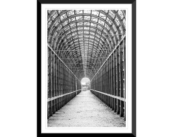 May include: A black and white photograph of a long, narrow, arched walkway made of wooden beams. The walkway is empty and leads to a bright light at the end.