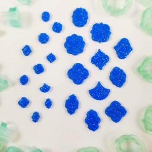 May include: A collection of blue glitter cookie cutters in various shapes, including a crescent moon, a four-leaf clover, a star, and a variety of geometric shapes.