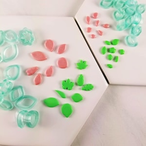 May include: A set of green and pink polymer clay leaf and flower shapes. The shapes are arranged on a white surface.