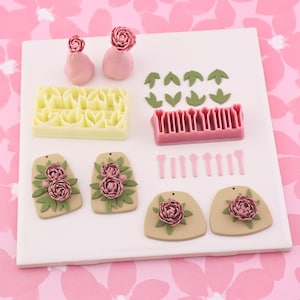 May include: A collection of polymer clay tools and finished pieces. Includes pink flower and leaf molds, a pink texture tool, and several finished earrings and pendants with pink flower and green leaf details. The items are arranged on a white surface.