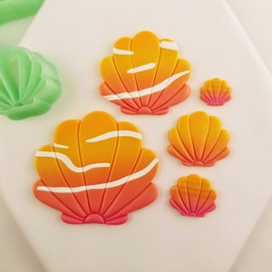 May include: A collection of colorful seashell-shaped decorations. The shells feature a gradient of orange and pink hues, with white stripes. The sizes vary, with some larger and some smaller. A green, shell-shaped decoration is also visible.
