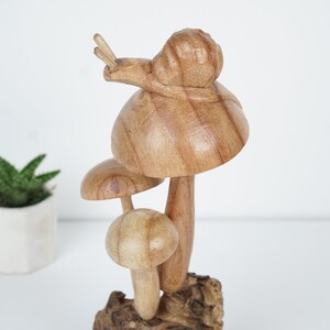 Puede incluir: Una escultura de madera de tres setas con un caracol en la parte superior. Las setas son marrones y tienen un acabado de madera natural. El caracol tambi&eacute;n es marr&oacute;n y tiene una concha detallada.