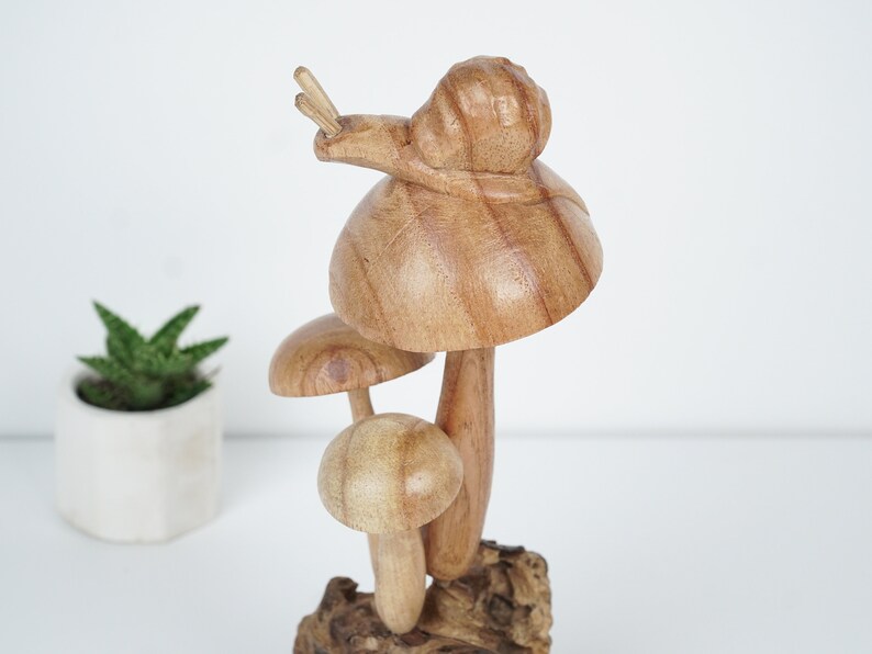 Puede incluir: Una escultura de madera de tres setas con un caracol en la parte superior. Las setas son marrones y tienen un acabado de madera natural. El caracol tambi&eacute;n es marr&oacute;n y tiene una concha detallada.