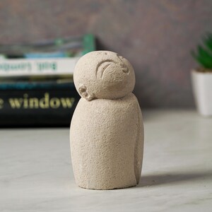 May include: A small, white, stone sculpture of a person with a simple, carved face. The sculpture is looking up and has a textured surface.