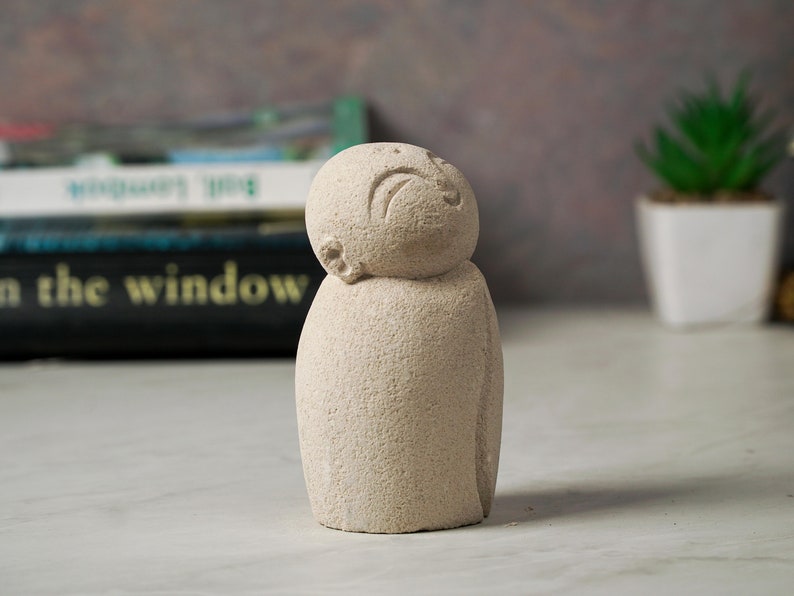 May include: A small, white, stone sculpture of a person with a simple, carved face. The sculpture is looking up and has a textured surface.