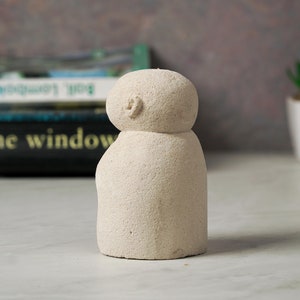 Puede incluir: Una peque&ntilde;a escultura de cer&aacute;mica blanca texturizada que representa a una persona con cabeza redonda y cuerpo simple y redondeado.