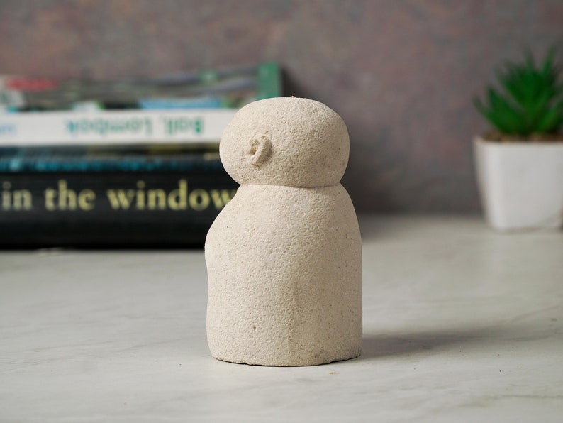 Puede incluir: Una peque&ntilde;a escultura de cer&aacute;mica blanca texturizada que representa a una persona con cabeza redonda y cuerpo simple y redondeado.