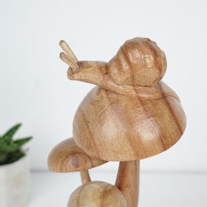 Puede incluir: Escultura de madera de un hongo con un caracol en la parte superior. El hongo es marr&oacute;n y tiene un tallo blanco. El caracol tambi&eacute;n es marr&oacute;n y tiene una concha blanca.