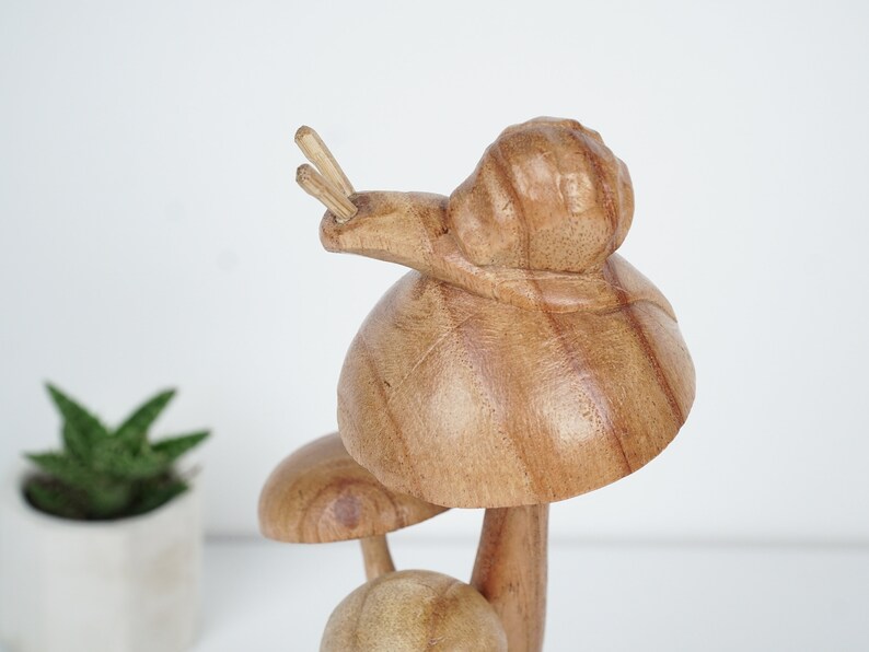 Puede incluir: Escultura de madera de un hongo con un caracol en la parte superior. El hongo es marr&oacute;n y tiene un tallo blanco. El caracol tambi&eacute;n es marr&oacute;n y tiene una concha blanca.