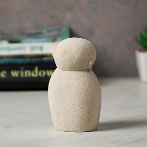 May include: A small, white, textured, ceramic sculpture of a person. The sculpture has a round head and a round body.