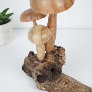 Puede incluir: Una escultura de madera de setas con tres setas apiladas una encima de la otra. Las setas est&aacute;n talladas en madera marr&oacute;n claro y tienen una veta de madera natural. La escultura est&aacute; sentada sobre un trozo de madera flotante.