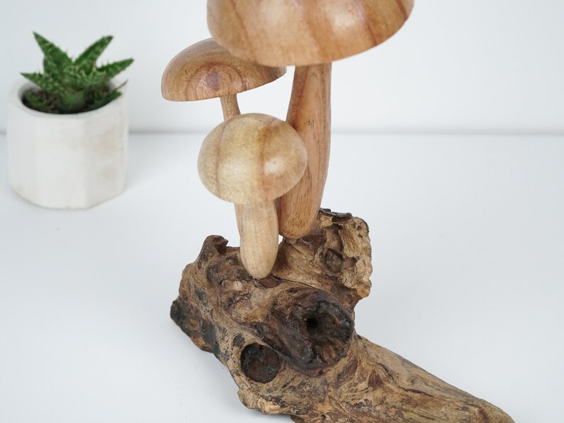 Puede incluir: Una escultura de madera de setas con tres setas apiladas una encima de la otra. Las setas est&aacute;n talladas en madera marr&oacute;n claro y tienen una veta de madera natural. La escultura est&aacute; sentada sobre un trozo de madera flotante.