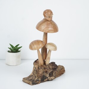 Puede incluir: Una escultura de madera de tres setas con un caracol en la parte superior de la seta m&aacute;s grande. Las setas est&aacute;n sobre una base de madera.