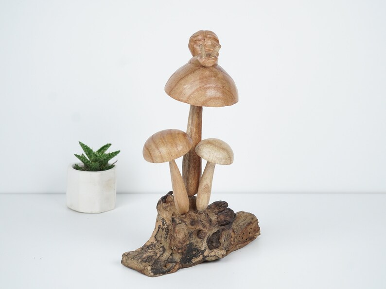 Puede incluir: Una escultura de madera de tres setas con un caracol en la parte superior de la seta m&aacute;s grande. Las setas est&aacute;n sobre una base de madera.