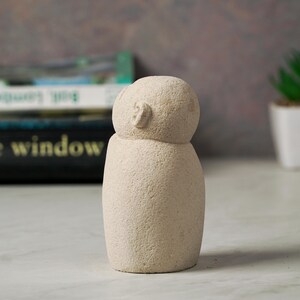 May include: A small, white, stone sculpture of a person with a rounded head and a simple, abstract face.