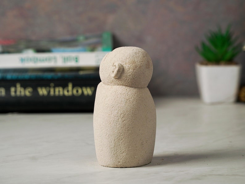 May include: A small, white, stone sculpture of a person with a rounded head and a simple, abstract face.