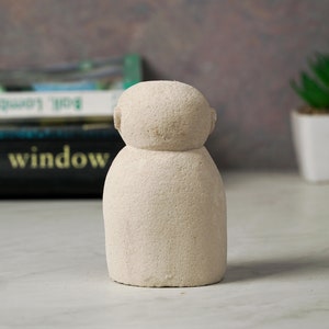 Puede incluir: Una peque&ntilde;a escultura de cer&aacute;mica blanca texturizada que representa a una persona con cabeza redonda y cuerpo simple y redondeado.