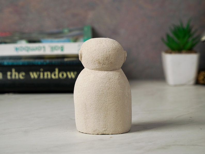 Puede incluir: Una peque&ntilde;a escultura de cer&aacute;mica blanca texturizada que representa a una persona con cabeza redonda y cuerpo simple y redondeado.