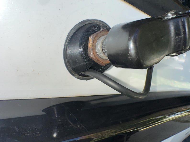 May include: Close-up of a black, rounded component attached to a white surface. A rusty nut and a black cable are visible. The component appears to be part of a larger mechanism.