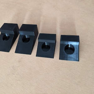 May include: Four black plastic corner protectors with a round hole in the center of each. The protectors are arranged in a row from left to right.